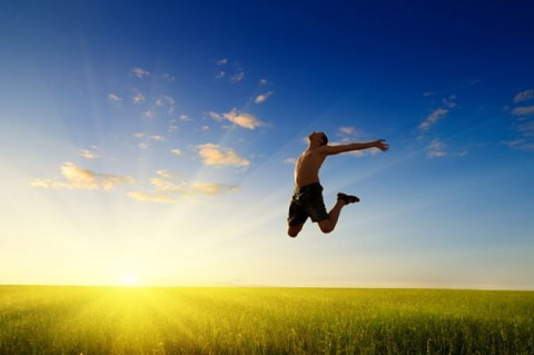 На фоне голубого неба и ярких лучей солнца фигура счастливого парня, застывшая в прыжке над зелёным полем. 